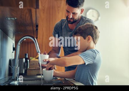 Brilla nei piatti con papà. Un padre e un figlio lavano i piatti insieme a casa. Foto Stock