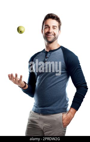 Sai quello che dicono... una mela al giorno... Studio ritratto di un bel giovane uomo che lancia una mela su uno sfondo bianco. Foto Stock