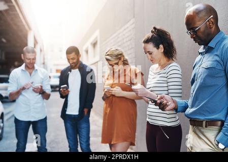 Gli uomini d'affari leggono messaggi al telefono, controllano le notifiche e scrivono messaggi online durante una pausa al lavoro. Gruppo di diversi colleghi che scorrono su Internet, navigano su app e utilizzano reti Foto Stock