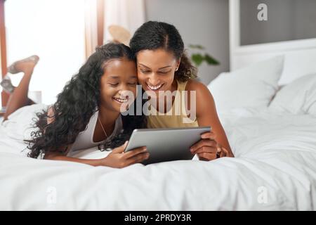 Guarda i nostri cartoni animati preferiti online. Mamma e figlia sdraiate a letto con un tablet digitale. Foto Stock