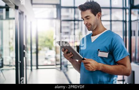 Aggiornare i suoi pazienti progressi sul suo dispositivo. Un giovane e bello medico maschile che lavora in un ospedale. Foto Stock