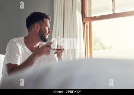 Sono grato di svegliarmi: Un bel giovane che beve caffè in camera da letto a casa. Foto Stock