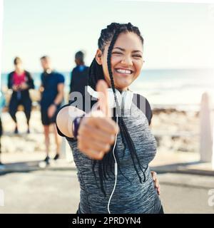 Youre bene sul vostro senso ad un voi migliore. Ritratto di una giovane donna sportiva che mostra i pollici in su mentre si esercita all'aperto. Foto Stock