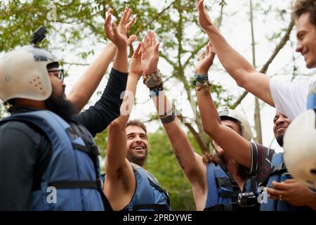 Questo è per essere un cercatore avventuriero. Un gruppo di giovani amici maschi che si danno a vicenda un alto cinque prima di andare rafting sulle rapide. Foto Stock