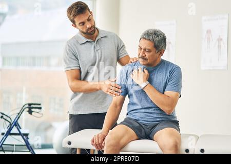 Dove fa male. Un giovane fisioterapista maschile che assiste un paziente anziano nel recupero. Foto Stock