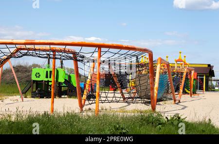 Moderno parco giochi pubblico contro il cielo blu. Un colorato complesso sportivo per bambini senza persone. Attrezzature per arrampicata su roccia e assalto al parco giochi. Foto Stock