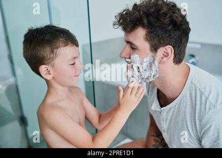 La barba è così cara papà: Un ragazzino che si strofinava la crema per rasare il viso dei padri nel bagno di casa. Foto Stock