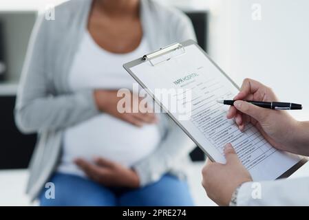 Tutto sembra essere in ordine: Un medico femminile irriconoscibile che si consulta con una paziente incinta in un ospedale durante il giorno. Foto Stock