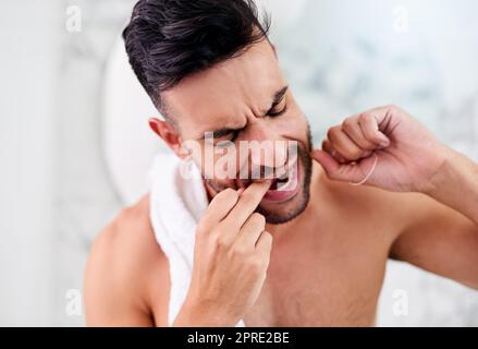 Fate attenzione a non far passare troppo il filo per evitare danni dentali. Un bel giovanotto che gli galleggia i denti in bagno. Foto Stock