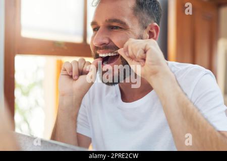 Fate un passo avanti nella vostra routine di igiene dentale con il filo del filo interdentale. Un bel giovanotto che gli gallina i denti in bagno. Foto Stock