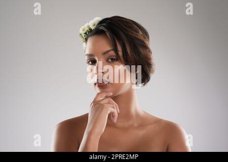 La bellezza viene naturalmente a lei. Studio ritratto di una bella giovane donna con fiori nei suoi capelli che si posano su uno sfondo grigio. Foto Stock