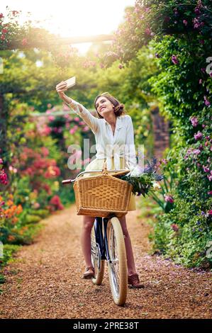 Cattura la bellezza di una giornata primaverile da cartolina. Una giovane donna attraente che prende un selfie mentre guida una bicicletta all'aperto. Foto Stock