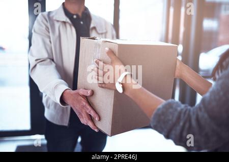 Consegnare i pacchi in modo sicuro è quello che faccio io. Un uomo irriconoscibile che consegna un pacco a un cliente all'interno di un ufficio durante il giorno. Foto Stock