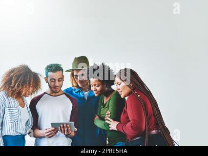 Vivere la vita virtualmente e in tempo reale. Studio di un gruppo di giovani che utilizzano un tablet digitale insieme. Foto Stock