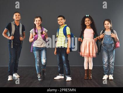 Oggi è l'inizio di qualcosa di nuovo. Studio ritratto di un gruppo diversificato di bambini che portano i loro zaini scuola su uno sfondo grigio. Foto Stock