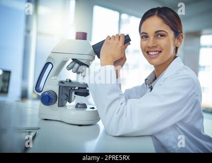 Scoprire curiosità attraverso la scienza. Ritratto di un giovane scienziato utilizzando un microscopio in laboratorio. Foto Stock