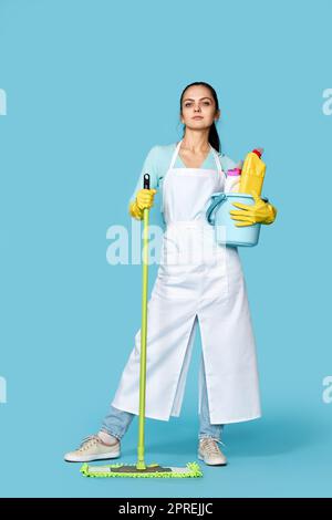 bella donna in guanti di gomma e grembiule più pulito con forniture di pulizia e spazzolone su sfondo blu Foto Stock