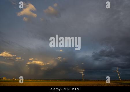 paesaggio pianeggiante con case due mulini a vento e raggi del sole tra fitte pendici Foto Stock