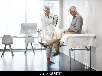 Così il suo ginocchio destro. Ripresa completa di una dottoressa matura che lavora con una paziente di sesso maschile anziano nel suo ufficio in ospedale. Foto Stock