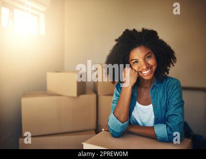 Meglio iniziare. Ritratto di una giovane donna allegra che riposa sulla sua mano mentre è circondata da scatole di cartone durante il giorno in movimento all'interno di casa. Foto Stock