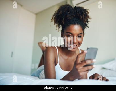 Io controllo sempre i miei social media prima di mattina. Una giovane donna bellissima che usa un cellulare nella sua camera da letto a casa. Foto Stock