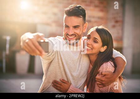 Amore prima di ogni altra cosa. Una giovane coppia felice che prende selfie insieme all'aperto. Foto Stock