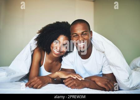 Questo è il modo in cui facciamo i fine settimana. Ritratto di una giovane coppia felice che si rilassa sotto un piumino nella loro camera da letto. Foto Stock