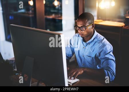 Niente migliora il business come mettere nelle ore. Un bel giovane uomo d'affari che usa un computer durante una tarda notte in un ufficio moderno. Foto Stock