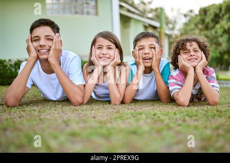 Chi ha bisogno del televisore quando si può divertirsi all'aperto. Ritratto di un gruppo di fratelli felici che giacciono insieme sull'erba nel loro cortile. Foto Stock