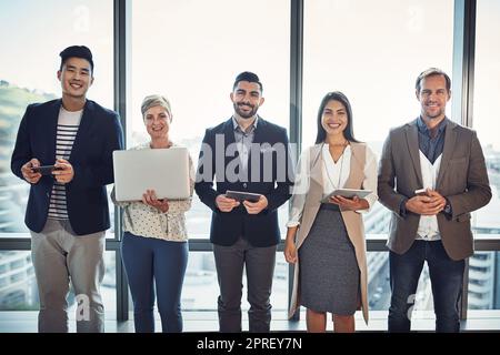 Il successo nell'era digitale. Ritratto di un gruppo eterogeneo di uomini d'affari che utilizzano la tecnologia wireless in un ufficio. Foto Stock