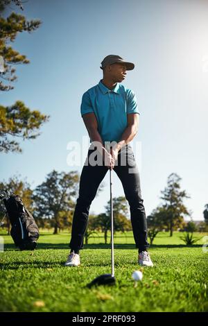 Guardando dove la palla andrà. Un giovane golfer maschio concentrato circa per oscillare e giocare un colpo con il suo golf club fuori su un campo. Foto Stock