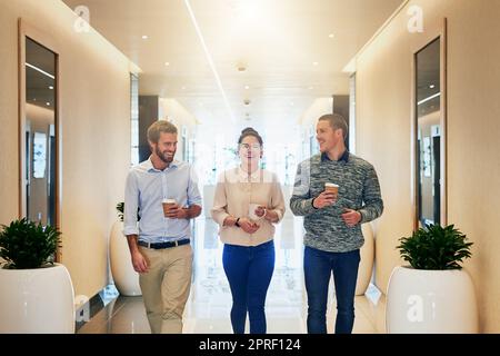 Anche i migliori hanno bisogno di una pausa di tanto in tanto. Ritratto di un gruppo di giovani uomini d'affari che camminano insieme lungo un passaggio mentre bevono caffè. Foto Stock