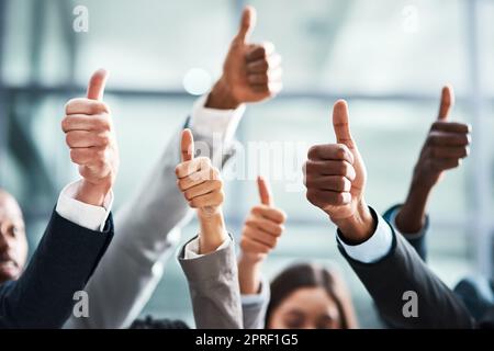 Continuate il grande lavoro. Primo piano di un gruppo di uomini d'affari che mostra i pollici in un ufficio. Foto Stock