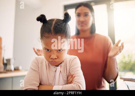 Bambina arrabbiata, infelice e sconvolta dopo la lotta o essere stata rimproverata dalla madre, disprezzandosi con l'atteggiamento e le braccia incrociate. Bambino cattivo che sembra offeso con genitori single stressati in background. Foto Stock