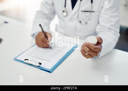 Compilazione di una nuova prescrizione. Colpo ad angolo alto di un medico maschio irriconoscibile che scrive su una forma mentre tiene il farmaco nel suo ufficio. Foto Stock