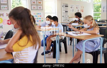 ... Imparare, insegnare la covid e studiare giovani studenti seduti in una classe scolastica al chiuso. Educazione di giovani, bambini e bambini con maschere che guardano e lavorano sul lavoro in classe in una pandemia. Foto Stock