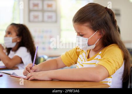 Ragazze scolastiche in classe, blocco dell'istruzione covid e distanza sociale. Gli studenti intelligenti disegnano e scrivono in modo creativo alle scrivanie imparando, indossando maschere a causa delle normative sulla malattia da coronavirus. Foto Stock