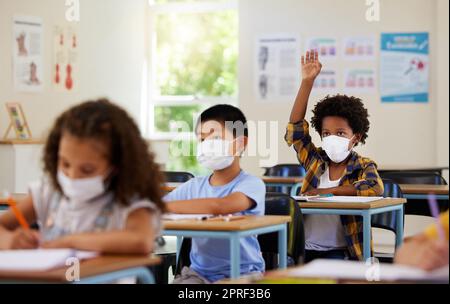 COVID, studenti e bambini dell'istruzione in classe scolastica che alzano la mano per rispondere, chiedere o mettere in discussione lezioni con i compagni di classe. Gruppo eterogeneo di bambini, ragazzi o ragazze con maschere facciali che imparano in classe di studio Foto Stock