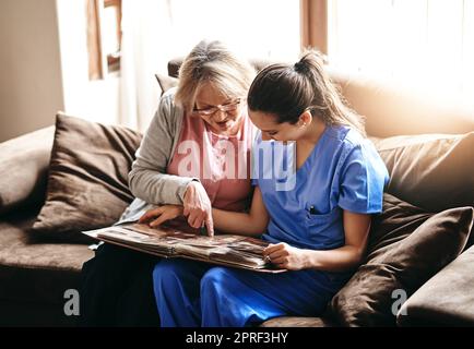 Scatenando alcuni vecchi ricordi, un'infermiera e una donna anziana che guardano insieme un album fotografico. Foto Stock