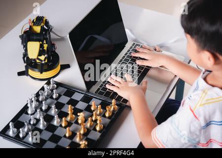 Codice di programmazione del bambino asiatico al braccio della macchina del robot sul laptop per giocare gli scacchi Foto Stock