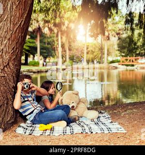 I bambini vedono sempre il divertimento nella vita: Due piccoli fratelli che si divertono mentre si siedono su una coperta al parco. Foto Stock