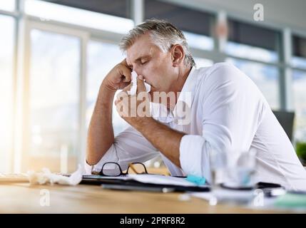 Potrei addormentarmi proprio qui. Un uomo d'affari maturo che soffia il naso in ufficio. Foto Stock