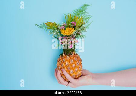 Chi dice che i fiori appartengono solo ai vasi: Una donna irriconoscibile che tiene un ananas farcito di fiori. Foto Stock