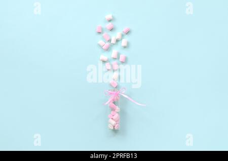 Rosa e Bianco marshmallow pezzi viene spruzzato da un piccolo contenitore di vetro su un pastello blu sullo sfondo. Piatto minimalismo laici. Vista superiore Foto Stock