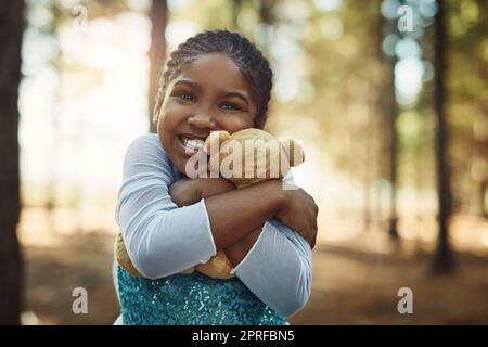 Coccole per la sua soffice amica. Ritratto di una bambina che gioca nel bosco con il suo orsacchiotto. Foto Stock