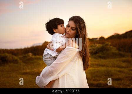 Le mie più grandi benedizioni mi chiamano mamma, un figlio bacia la giovane madre sulla guancia all'aperto. Foto Stock