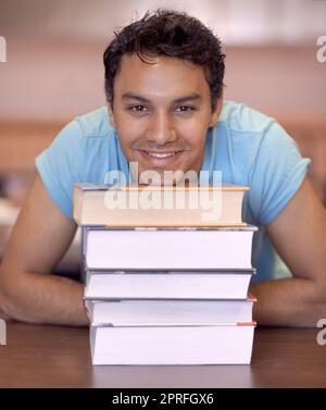 HES desideroso di imparare. Ritratto di un giovane seduto e poggiato la testa su alcuni libri di testo Foto Stock