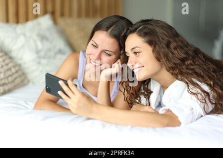 Due amici che controllano il telefono su un letto dell'hotel Foto Stock