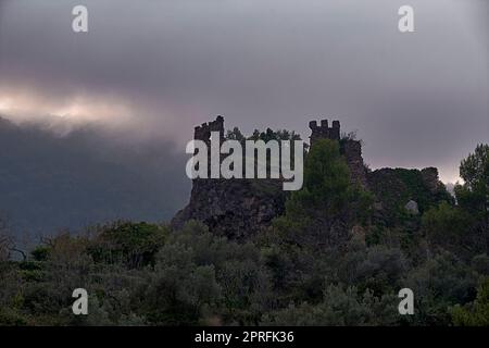 Jinquer, Castellon, Spagna. Rovine di un castello abbandonato in cima alla foresta di mountain.Mediterranean, ulivi, pini, cielo con nuvole tempesta Foto Stock