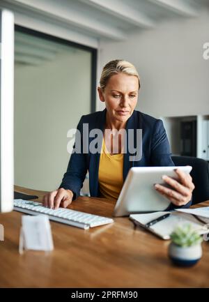 Utilizzare la tecnologia moderna per portare a termine il lavoro. Una donna d'affari matura che lavora su un tablet nel suo ufficio aziendale. Foto Stock
